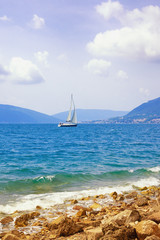 Obraz premium Beautiful Mediterranean landscape. One sailboat with white sail on water. Montenegro, Adriatic Sea. View of Kotor Bay near Tivat city. Travel concept