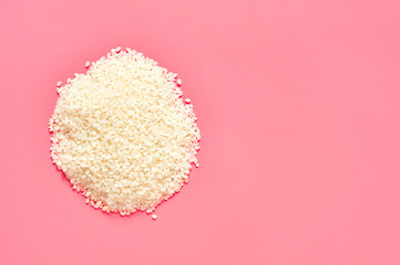 Heap of grain of white rice on pink background. Copy space. Top view