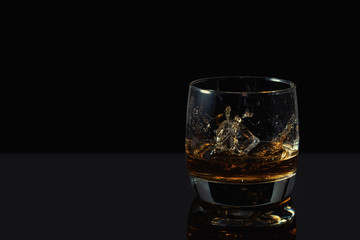 Whiskey splash in glass with ice on a dark background