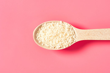 Wooden spoon with grain of white rice on pink background. Top view
