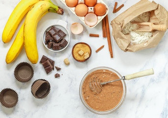 Preparation of dough for homemade muffins with banana and chocolate drops for Breakfast. Ingredients on the table - wheat flour, eggs, brown sugar, chocolate chips, fresh fruit, cinnamon