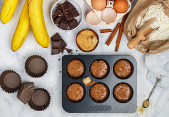 Preparation homemade muffins with banana and chocolate for Breakfast. Ingredients on the table - wheat flour, eggs, brown sugar, chocolate chips, fresh fruit, cinnamon. Selective focus, top view