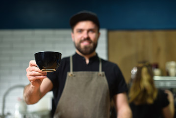 A young bearded barista bartender offers a large cup of coffee. Small business concept.