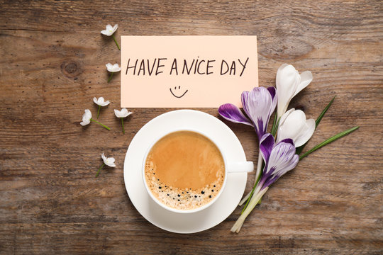Morning coffee, flowers and card with HAVE A NICE DAY wish on wooden table, flat lay