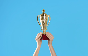 Woman holding gold trophy cup on light blue background, closeup