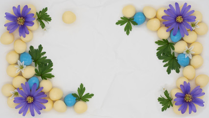 Blue and white flowers green leaves and candy Easter eggs on a scrunched plain white paper background with copy space