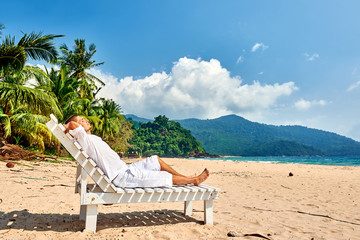Man in white relaxing in sun bed on beach