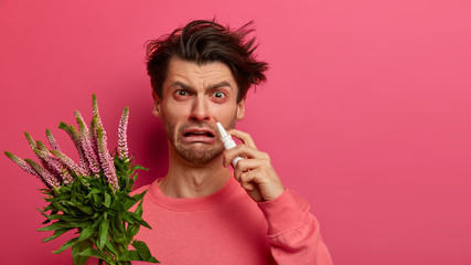 Indoor shot of frustrated man has watery red eyes, runny stuffy nose, uses drops, suffers from hay...