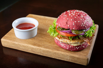 Red burger with cutlet and vegetables on a cutting wooden board.