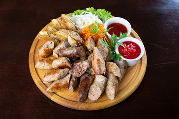 Homemade grilled sausages with sauerkraut and ketchup on a round wooden tray.