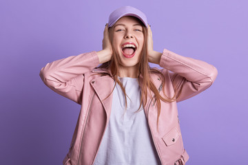 Attarctive woman in leather pink jacket covering ears and feeling irritation from loud repairing works, expressing dislike, looking directly at camera, screaming something. People emotions concept.