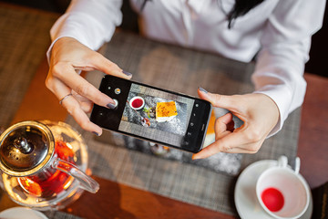 Female Hands Holding mobile Phone and Taking Photo of cake in cafe. Flat lay, top view, overhead. Blogger lifestyle