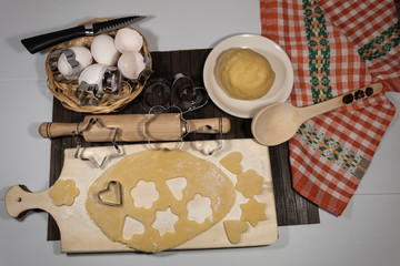 View from above. On the table is a dough, eggs, cookie molds. On the cutting board lies rolled dough and cookies of various shapes are squeezed out of it.
