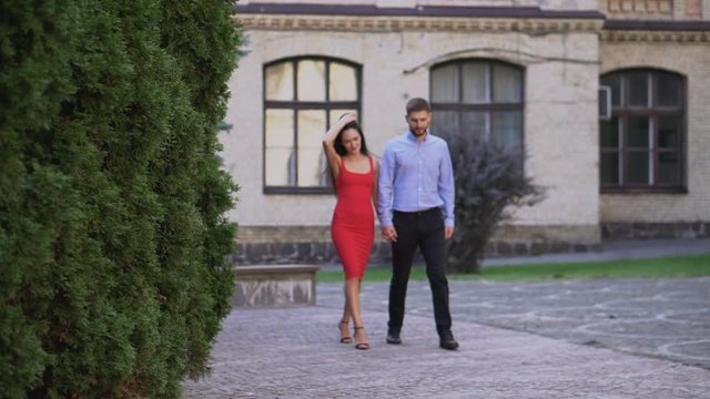 Beautiful couple Boyfriend and girlfriend walking and kissing on a park background. Man and woman love. Girl in a red dress and a guy.
