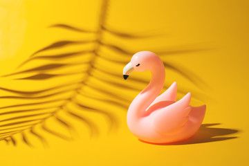 Summer vacation concept with toy flamingo on yellow background, creative pastel