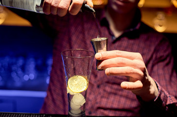 A male bartender in a nightclub at work preparing a cocktail in a large glass.