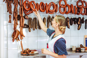 Saleslady getting sausages from the hook in butchery shop
