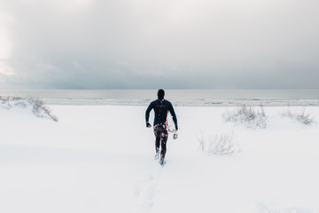 Cold winter and male surfer with surfboard. Snowy weather day with surfer in wetsuit.