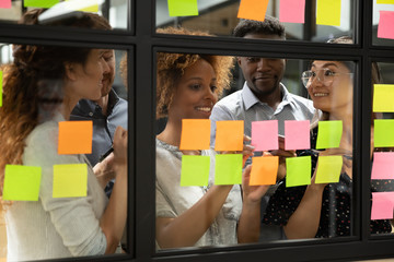 African American leader with diverse employees team writing creative ideas, tasks on sticky papers...