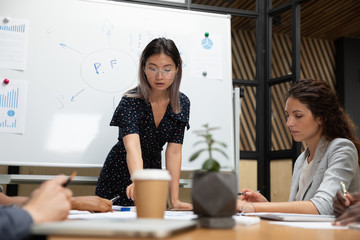 Confident Asian businesswoman in glasses holding briefing with diverse employees, mentor coach...