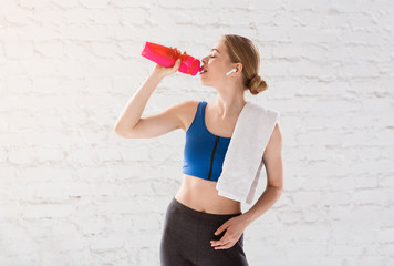 Young gymnast or dancer drinking water from plastic bottle after training against white wall