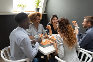 Excited diverse employees team eating pizza at lunch break, having fun, chatting, laughing at joke, happy colleagues, friends eating Italian fast food, sharing meal, good friendly relationship