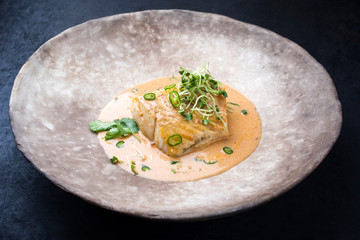 Gebratenes Skrei Kabeljau Fisch Filet in Thai Curry mit Chili und Sprossen als closeup auf einem Modern Design Teller