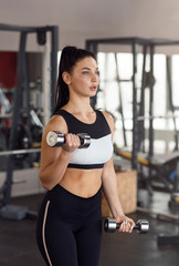 Fototapeta na wymiar Sporty girl exercising with dumbbells in gym