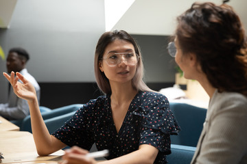 Serious Asian businesswoman wearing glasses sharing ideas, brainstorming, discussing project with...