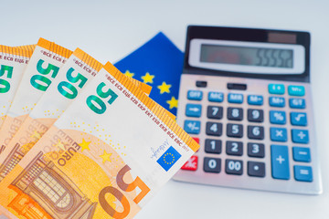 Euro banknotes on the background of the calculator and the EU flag. Finance of the Euro zone countries. Wages and taxes in the countries of the European Community.