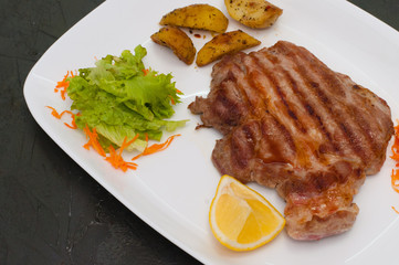Grilled meat steak with lemon, carrots, lettuce and potatoes. Juicy and very tasty dish of Italian cuisine