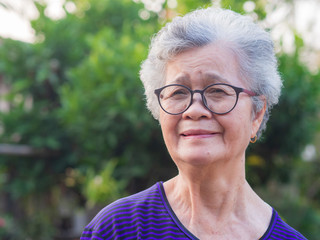 Close-up of face elderly woman smiling happiness, short white hair and looking at the camera, standing in garden. Asian senior woman healthy and have positive thoughts on life make her happy every day