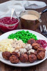 Traditional swedish meatballs served with mashed potato, green peas, cream sauce and cranberry jam, on plate, vertical