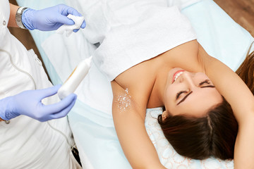 Happy young girl in a beauty salon smiling during a hair removal procedure. A professional cosmetologist performs sugaring work.