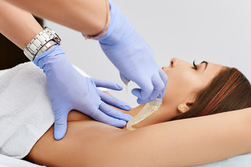 Beautician in a beauty salon, applies paste on client's armpits. Young girl on a sugaring procedure.
