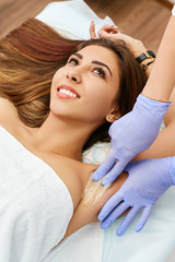 Beautician does shugaring axillary body part of a young brunette. The girl in the beauty salon is smiling.