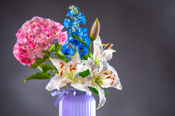 Bouquet of garden flowers close-up. Lily, delphinium and hydrangea in a lilac vase. Bouquet of...