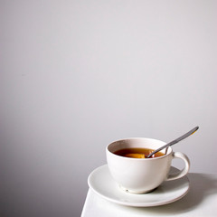 White cup of tea with lemon with a saucer and spoon on a white table. Vertical frame. Empty space