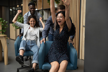 Excited businesswomen riding on chairs, laughing and shouting, diverse colleagues having fun in...