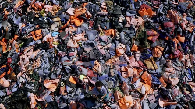 Drone flying over man showing scale of refugee crisis at Huge piles of lifejackets of refugees at lifejacket graveyard in Lesbos, Greece. plastic pollution and refugee crisis. EU turkey deal