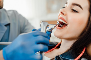 Cropped image. Happy young  woman lying with opened mouth. Male dentist in blue gloves using restoration instruments.