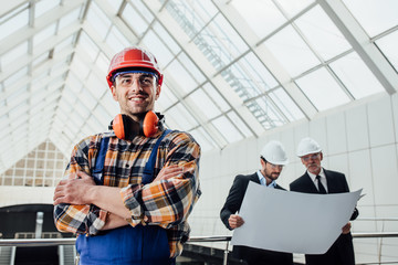 Worker with red helmet crossed arms, wear in jeans shirt near a industrial  fabric wall.