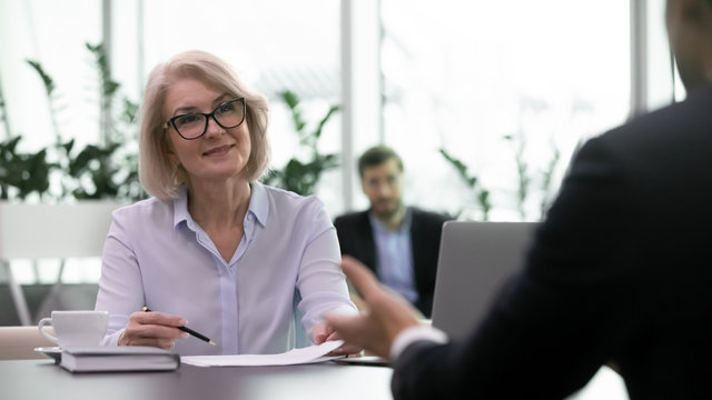 Smiling middle-aged businesswoman lead interview with male job candidate listening, happy senior female boss satisfied with man work applicant during hiring process, employment concept