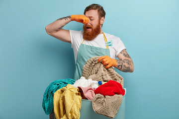Redhead man covers nose, feels bad smell, disgusting aroma from dirty laundry, going to wash with...