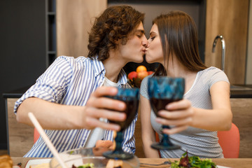 Romantic evening, couple kissing at home kitchen with wine glasses