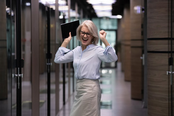 Overjoyed middle-aged businesswoman stand dance in modern company office corridor, happy senior female boss or employee feel excited celebrate successful project or have Friday fun, success concept