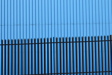 Steel Fence in front of Corrugated Steel Wall of Industrial Building painted Blue 