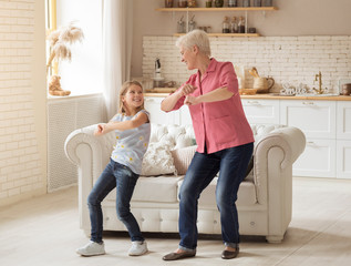 Cheerful older lady with her granddaughter dancing at home