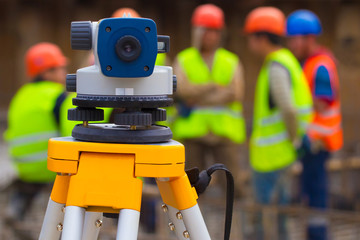 Theodolite on a tripod against the background of Builders in helmets and reflective vests. The use of theodolite in the construction. A device for measuring angles. Cartographic technique.