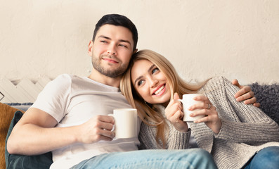 Handsome guy and his girlfriend with hot drinks spending time together at home, panorama